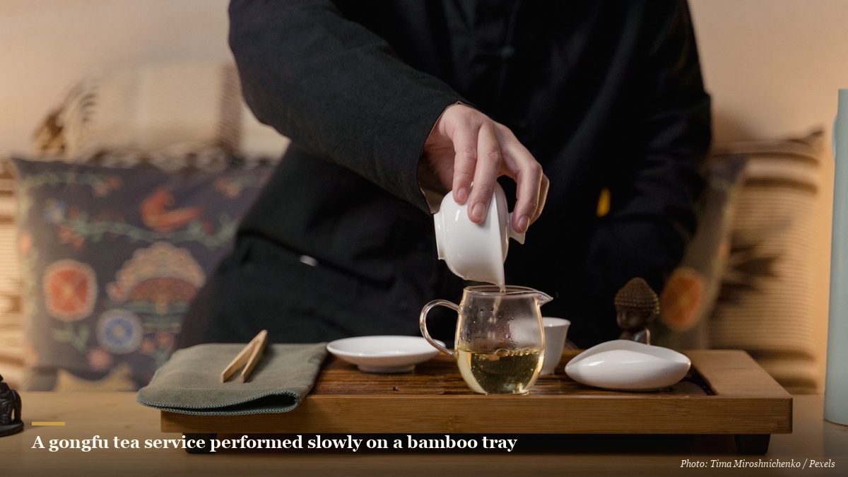 A person performing a gongfu tea service on a bamboo tray