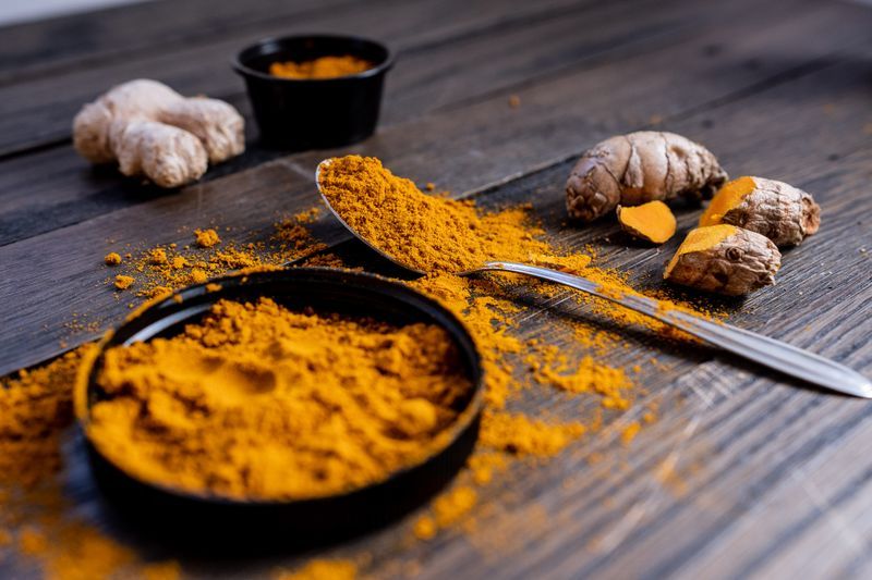Fresh turmeric root and golden turmeric powder on a wooden surface