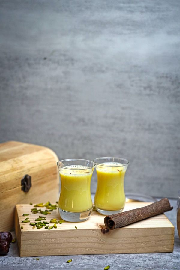 Two glasses of golden turmeric milk with cinnamon and pistachios on a wooden surface