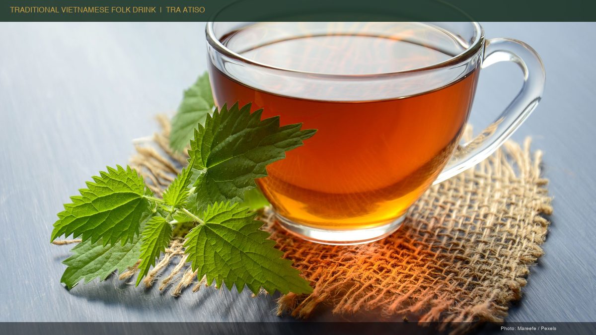 Glass cup of herbal tea on burlap mat beside fresh green leaves, representing traditional Vietnamese folk drink tra atiso