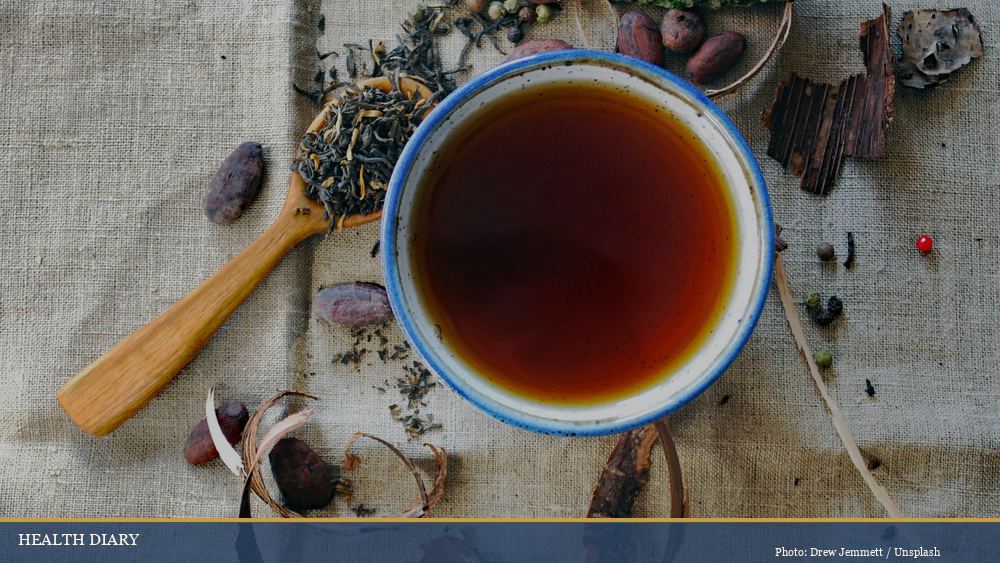 Bowl of dark amber herbal tea infusion surrounded by dried roots and bark ingredients overhead view