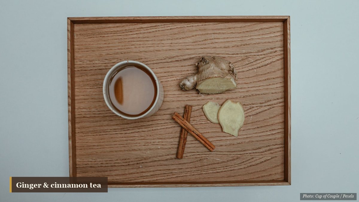 Overhead cup of ginger tea with fresh ginger root and cinnamon sticks on a wooden tray