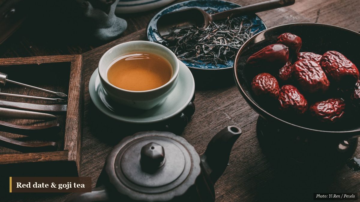 Amber red date tea in a pale cup beside a bowl of dried jujubes and a dark clay teapot