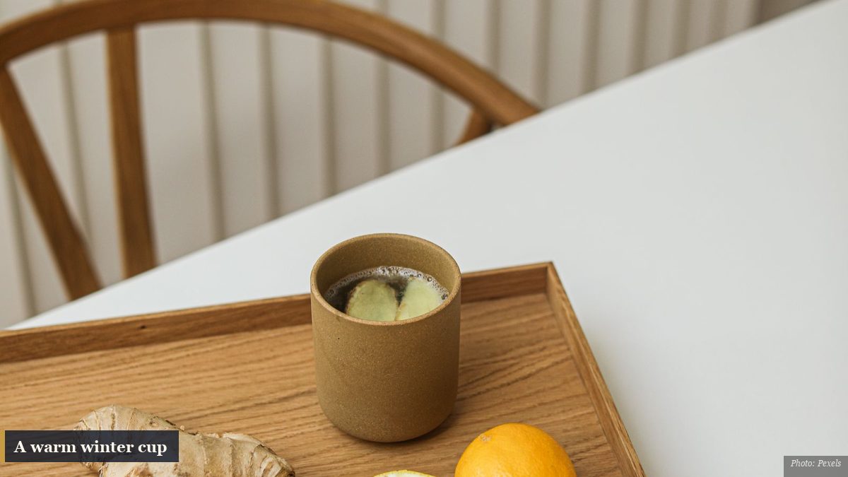 Warm cup of ginger tea on a wooden tray with fresh ginger root and lemon