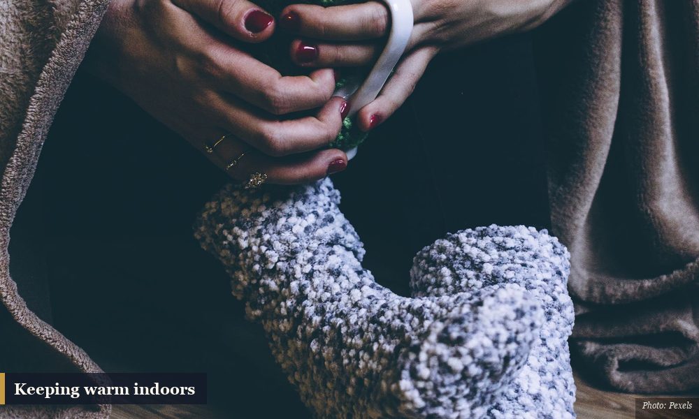 Person wrapped in a blanket wearing warm knit socks and holding a hot drink