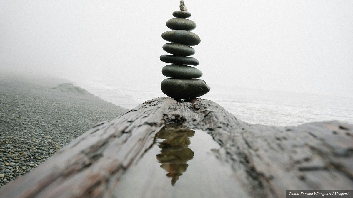 Stacked balancing stones reflected in still water on a foggy beach