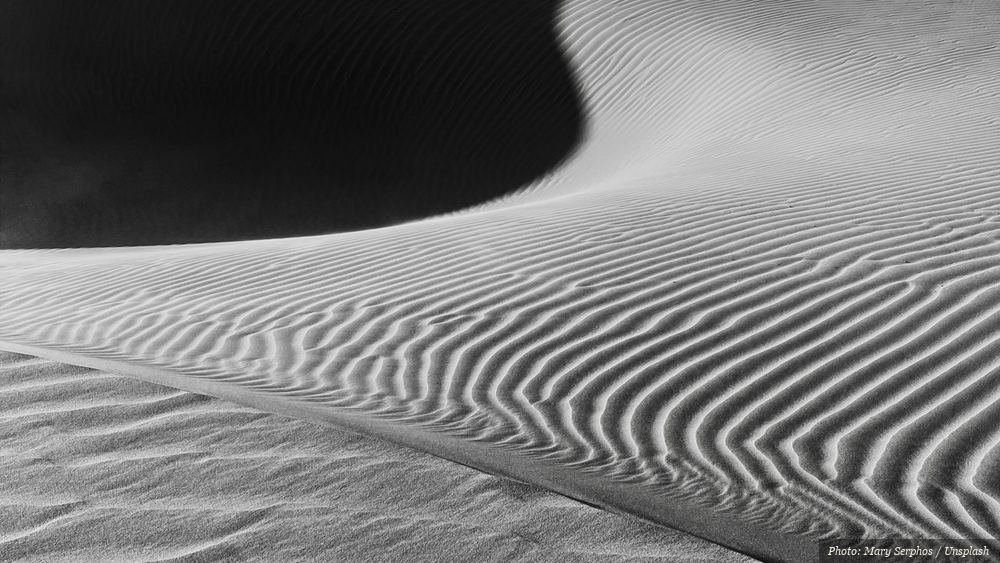 Curving line of light and shadow across rippled sand dunes