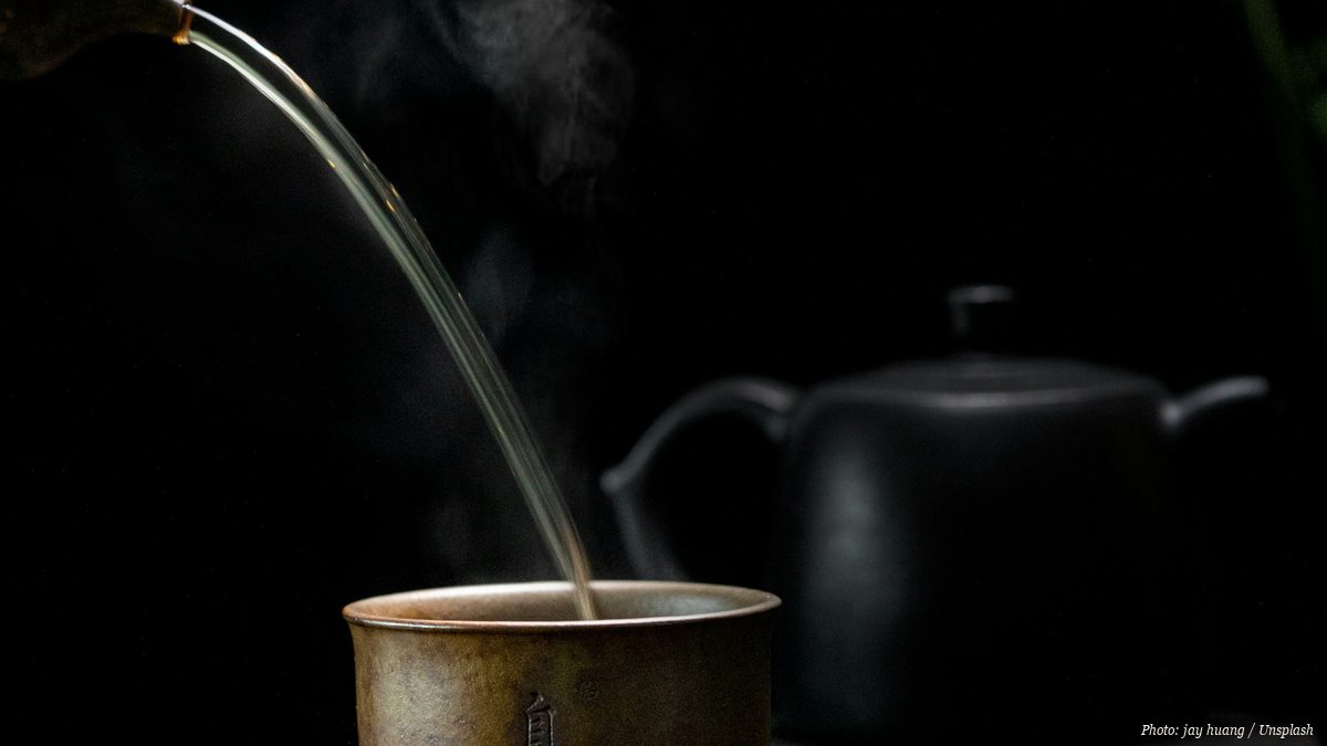 Steaming tea poured into a ceramic cup against a dark background